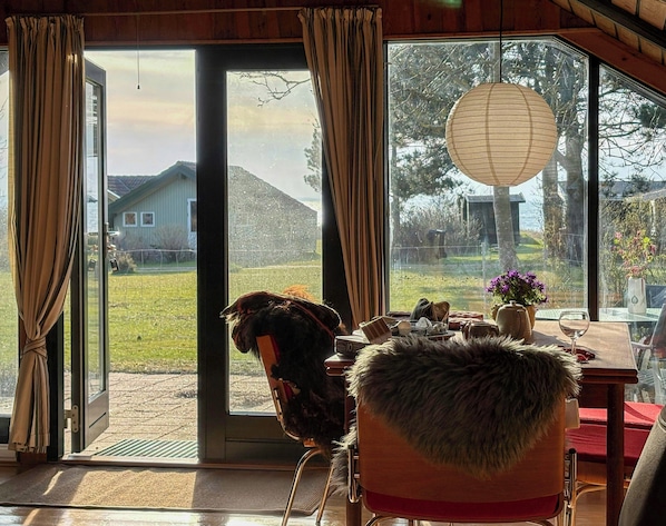 Ein Zimmer mit einer großen Schiebeglaswand, einem Sessel mit einem Fellüberwurf, einem Tisch mit Blumen und einer hängenden Papierlaterne.