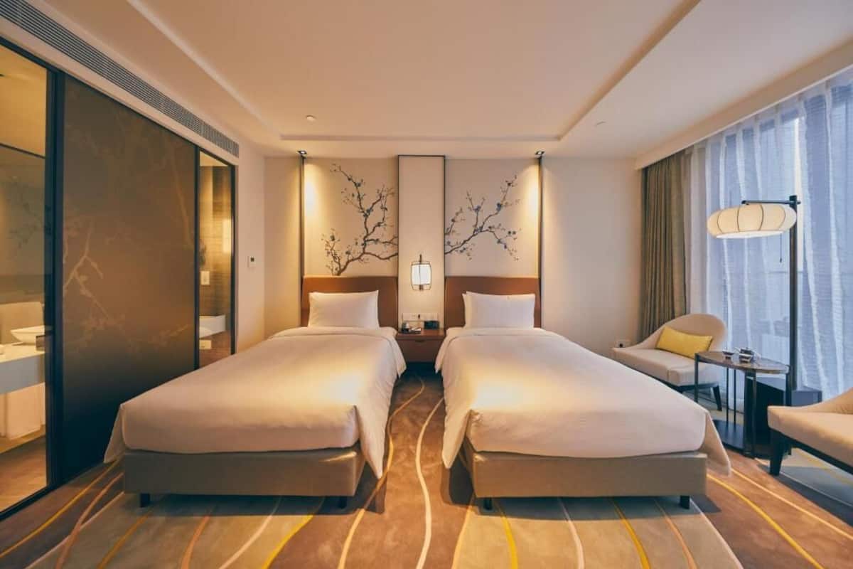 A hotel room with two beds, a sofa, a small table, and a large window with curtains.