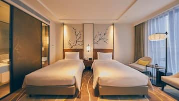 A hotel room with two beds, a sofa, a small table, and a large window with curtains.