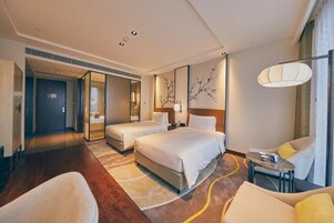 A hotel room with two beds, a sofa, a small table, and a large window.