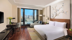 Habitación de hotel con una cama grande, un escritorio con silla, televisor y vista a la ciudad.