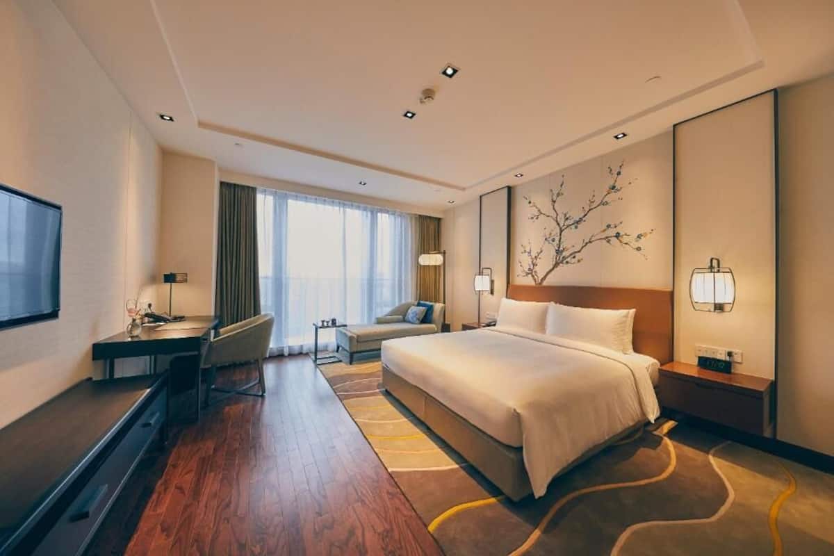 A hotel room with a bed, desk, chair, and a TV.