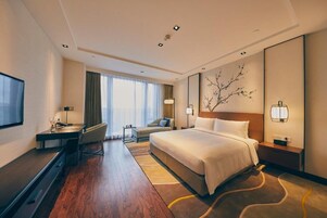 A hotel room with a bed, desk, chair, and a TV.