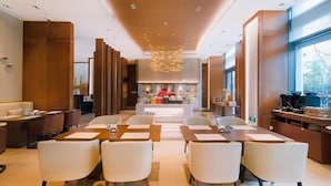 Un lobby moderno de hotel con un área de estar central, un mostrador de recepción y vista a la cocina en el fondo.
