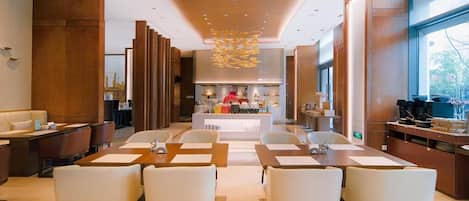 Een moderne hotellobby met een centraal zitgedeelte, een receptiebalie en een uitzicht op de keuken op de achtergrond.