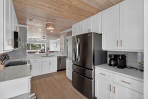A modern kitchen with white cabinetry, stainless steel appliances, and a wooden ceiling. - Shared Pool + Pickleball Court + Sunroom | Walk to the Beach | Isle Be There (Isle Of Palms)