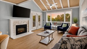 Ein Wohnzimmer mit Kamin, Fernseher, Deckenventilator und Blick ins Freie.
