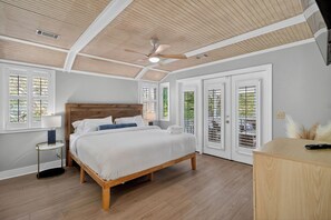 A bedroom with a wooden bed, a ceiling fan, and a view through the window. - Shared Pool + Pickleball Court + Sunroom | Walk to the Beach | Isle Be There (Isle Of Palms)