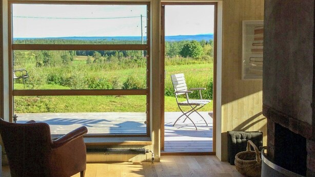 Una habitación con un ventanal grande, chimenea, una silla y una mesa.