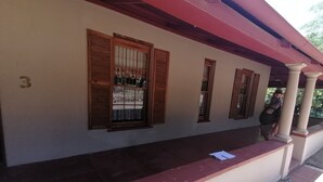 A building with a covered porch, wooden shutters on windows, and a tiled floor.