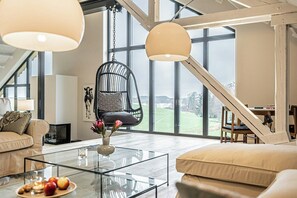 A spacious loft with a high ceiling, large windows, a hanging chair, a glass coffee table, and a cozy seating area. - Traditional architecture meets modern design (Thumby)