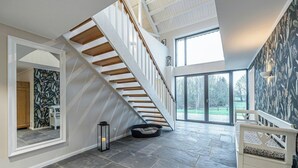 Une pièce spacieuse avec un escalier moderne, une grande fenêtre et un mur orné d’un motif.