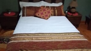 A bed with a patterned bedspread, pillows, and a headboard. There are two nightstands with lamps and a small table with a plant.