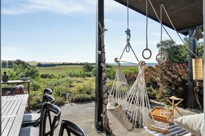 Eine Hängematte, ein Holztisch und Stühle auf einer Terrasse mit Blick auf ein Feld und Bäume.