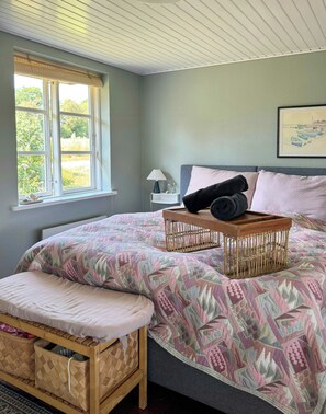 Ein Schlafzimmer mit Bett, Fenster, Nachttisch und einem an der Wand hängenden Bild.