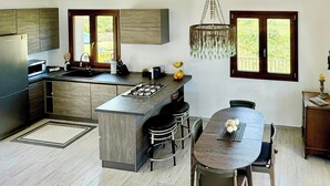 A modern kitchen with a central island, bar stools, a dining table, and a chandelier. - Sea view villa with panoramic pool near Scopello (Castellammare del Golfo)
