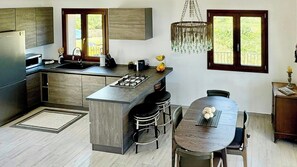 Eine moderne Küche mit einer zentralen Kochinsel, Barhocker, einem Esstisch und einer Deckenleuchte.