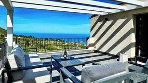 A covered outdoor seating area with a view of the sea, a table with a bottle and glasses, and a sofa. - Sea view villa with panoramic pool near Scopello (Castellammare del Golfo)