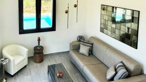 A living room with a sofa, a chair, a small table, a decorative object, and a window with a view of a pool. - Sea view villa with panoramic pool near Scopello (Castellammare del Golfo)
