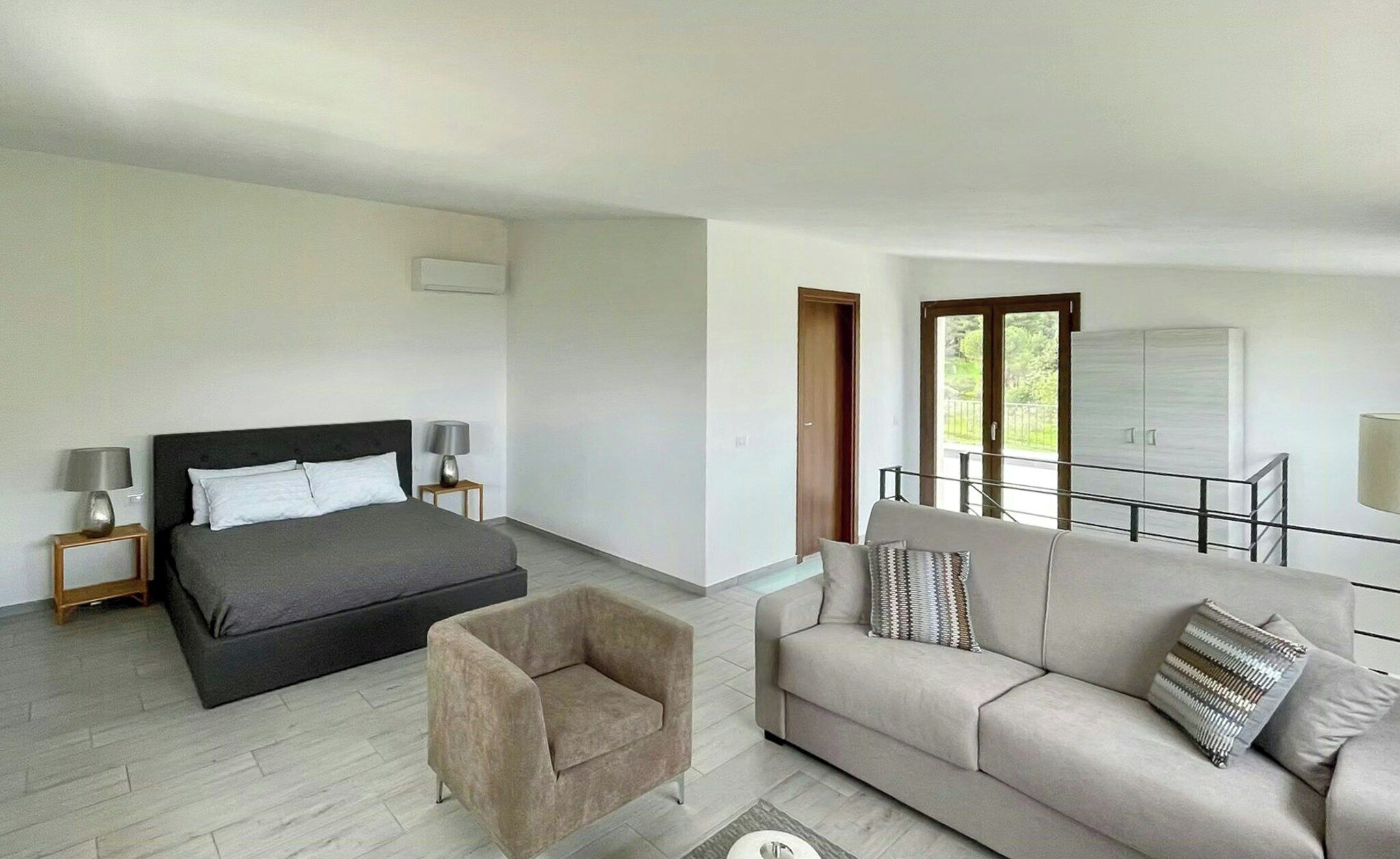 Un dormitorio moderno con cama, sofá, sillón y balcón con barandilla.