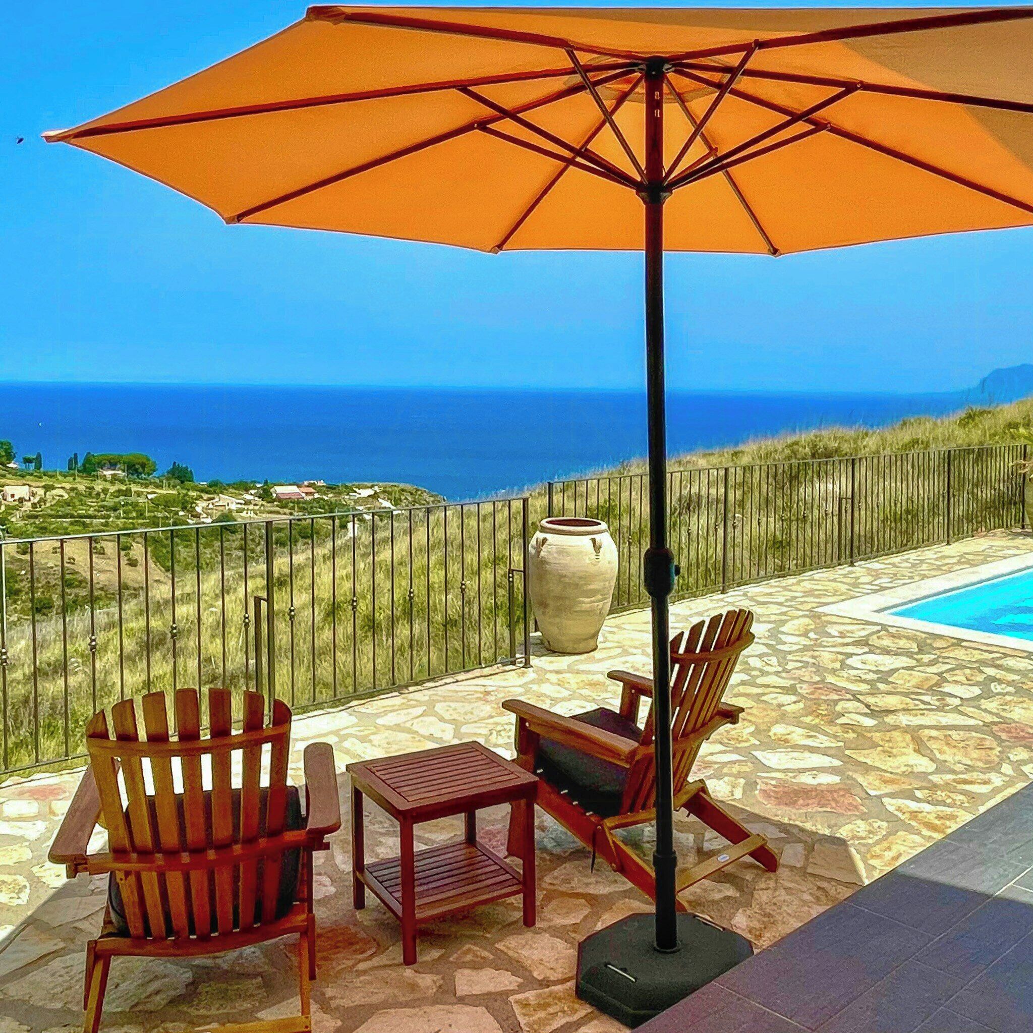 Un patio con due poltrone Adirondack, un tavolino e un ombrellone. Si vede una piscina sullo sfondo.