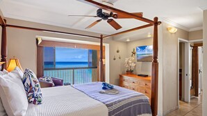 A four-poster bed with a ceiling fan, a view of the ocean, a wooden dresser, and a door leading to another room. - Oceanfront Corner-Unit, Large Lanai, Amazing Sunsets, Views! (Lahaina)