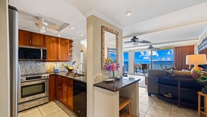 A modern kitchen with granite countertops, wooden cabinets, and stainless steel appliances. - Oceanfront Corner-Unit, Large Lanai, Amazing Sunsets, Views! (Lahaina)