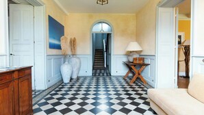A hallway with a checkered floor, white doors, a staircase, and a lamp on a wooden table. - 18th-century estate between Bordeaux and Sauternes (Saint-Côme)