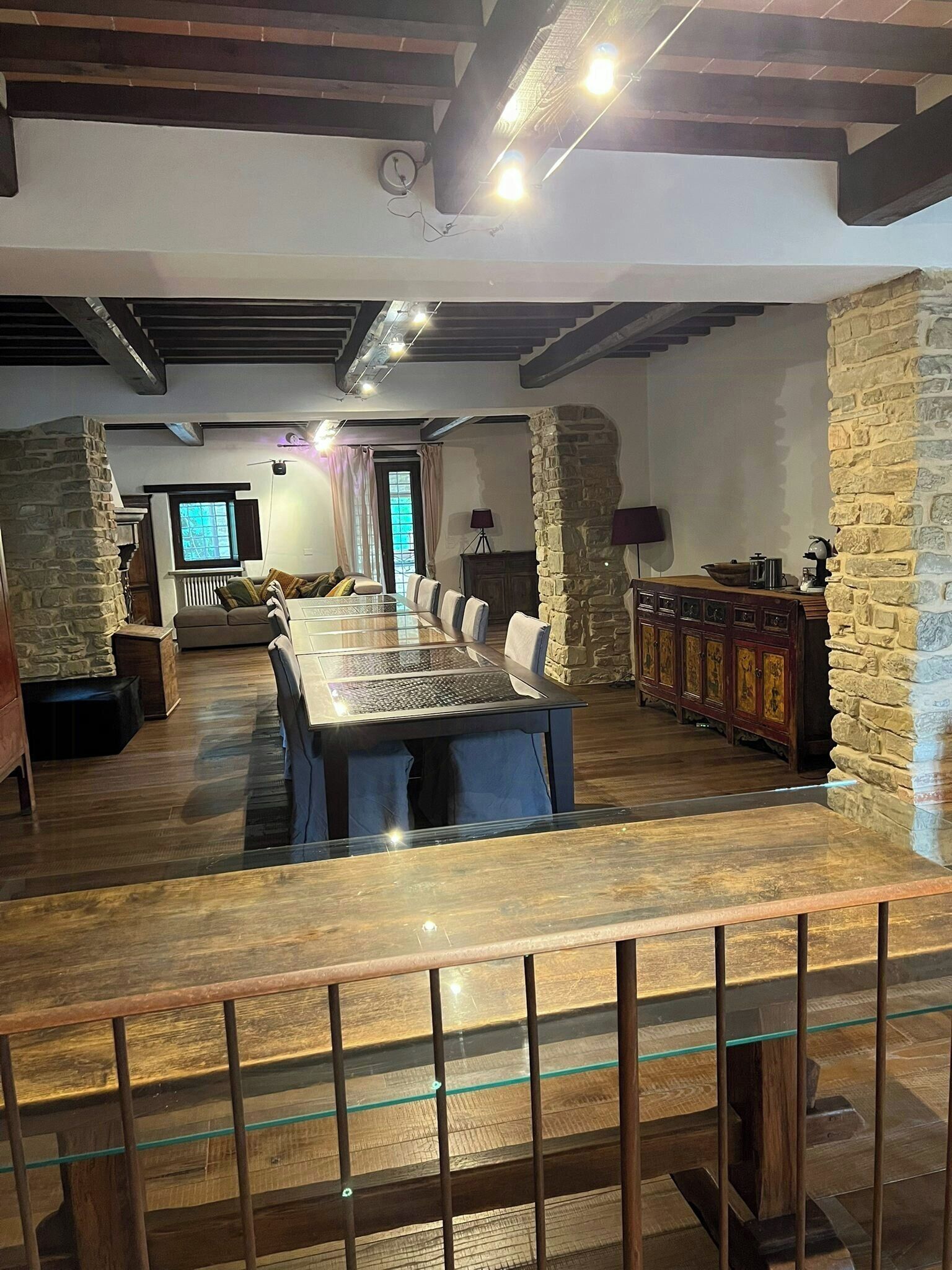 A spacious room with a long dining table, stone walls, and exposed wooden beams.