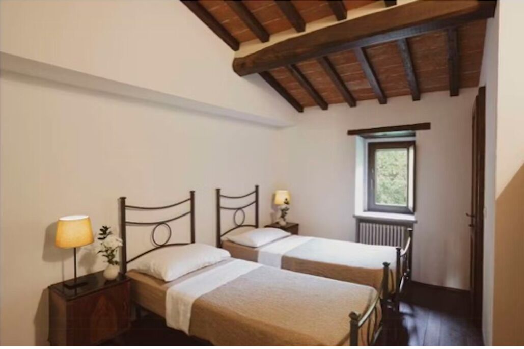 Una habitación con dos camas, una ventana, un radiador y techo de madera.