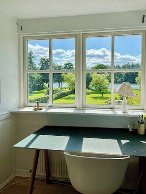 Ein Zimmer mit großem Schreibtisch, einem Stuhl und einem Fenster mit Blick auf eine grüne Landschaft.