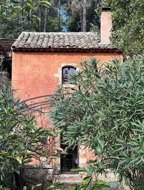A rustic building with a tiled roof, a small window, and a stone wall. - Bohemian house overlooking Roussillon (ROUSSILLON)