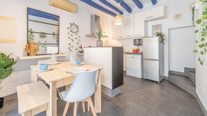 A modern kitchen with white cabinets, a central island, and a dining area with a wooden table and chairs. - CASA DE PUEBLO en el CENTRO de Roses, al lado de la playa con TERRAZA (Roses)