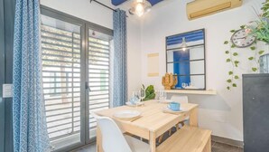 A dining area with a table set for two, a window with blinds, and a wall-mounted clock. - CASA DE PUEBLO en el CENTRO de Roses, al lado de la playa con TERRAZA (Roses)