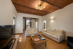 A spacious living area with a wooden ceiling, a sofa, a coffee table with books, and a television. - Villa with pool in the Arezzo countryside (Arezzo)