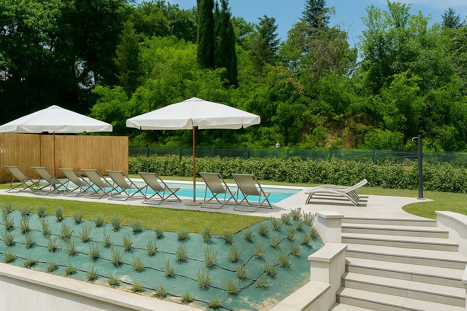 A pool area with lounge chairs and umbrellas, surrounded by greenery and a wooden fence.
