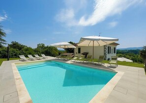 A swimming pool with lounge chairs and umbrellas, a small building with a sloped roof, and a view of the landscape. - Villa with pool in the Arezzo countryside (Arezzo)