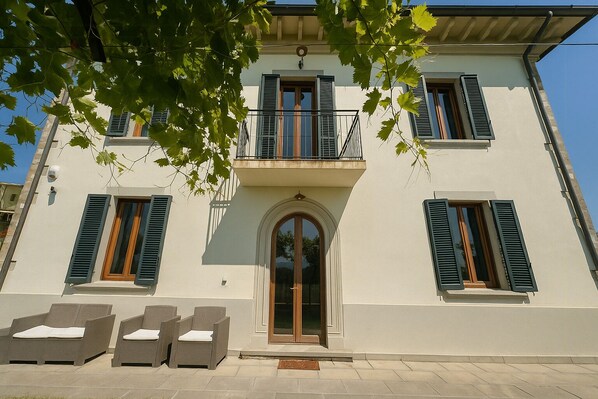 A two-story building with a balcony, a large arched entrance, and outdoor seating. - Villa with pool in the Arezzo countryside (Arezzo)