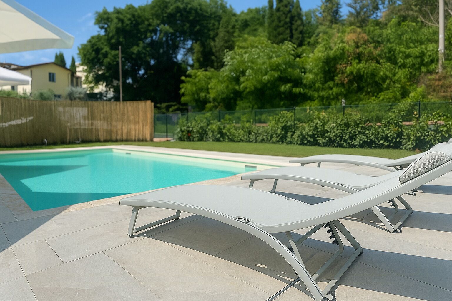 Piscina com duas espreguiçadeiras e um cercado de madeira ao fundo.