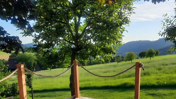 Un pontile in legno con due poltrone da relax, una ringhiera in corda e vista su un prato e colline lontane.
