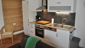 Una cucina compatta con mobili bianchi, una parete in legno, forno integrato e lavello.
