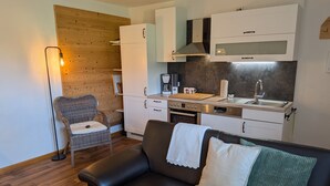 Una cucina moderna con mobili bianchi, forno integrato e lavello. Si vede una sedia in vimini e un divano in pelle nera con un cuscino verde.
