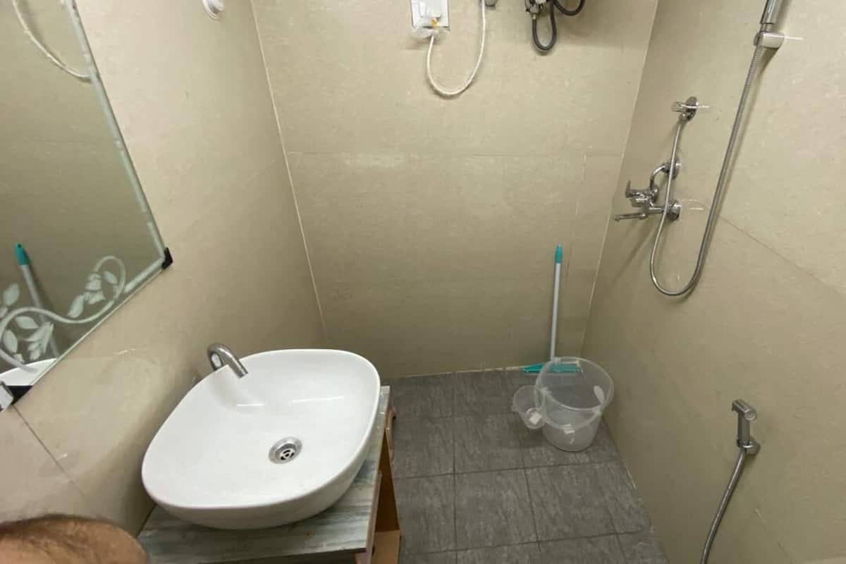 Une petite salle de bain avec un lavabo, un miroir, une douche et un récipient en plastique posé sur le sol.