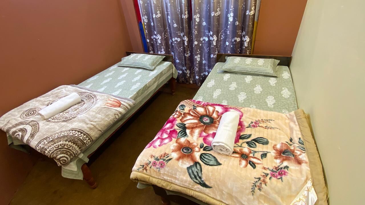 Dos camas individuales con cubrecamas florales, una cortina estampada con motivos florales y una pared lisa.