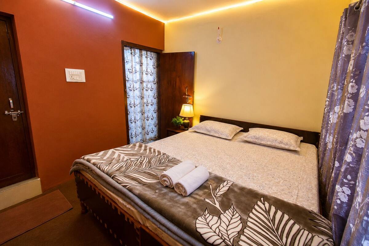 Une chambre d’hôtel avec un lit, une table de chevet, une lampe, une fenêtre avec des rideaux et une porte.