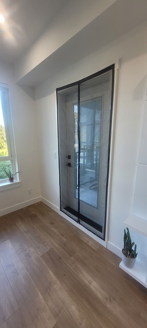 Quarto com porta de vidro deslizante, piso de madeira, uma janela com planta e um pequeno vaso com planta no chão.