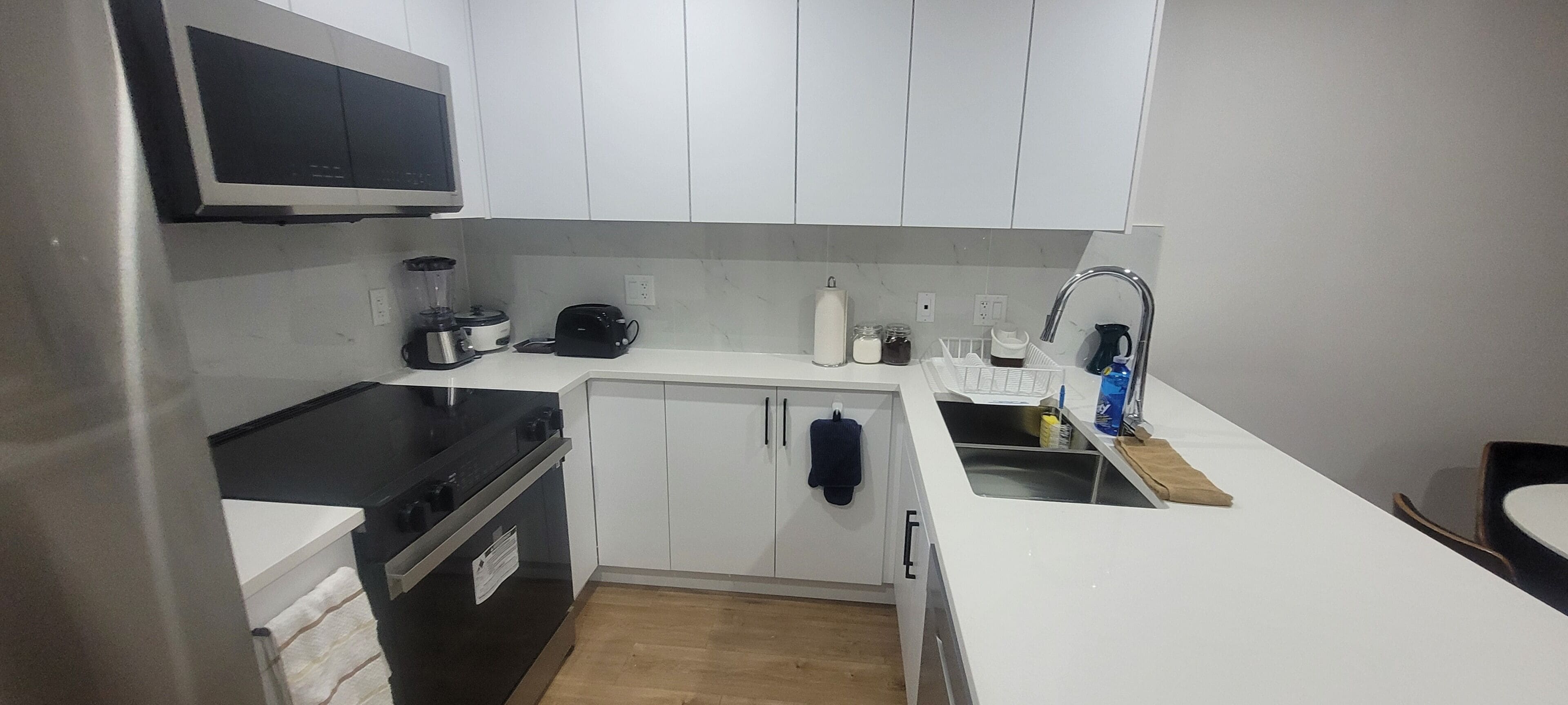 Een kleine keuken met witte kastjes, een zwart fornuis, een magnetron, een spoelbak en een broodrooster.