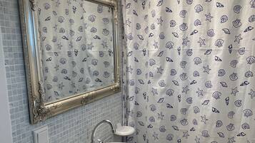 A bathroom with a tiled wall, a sink with a faucet, a mirror with an ornate frame, and a shower curtain with a sea shell pattern.