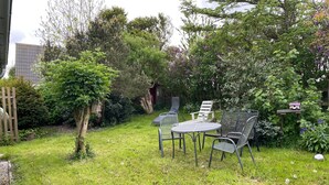 Un giardino con tavolo e sedie, immerso nel verde e delimitato da una recinzione in legno.