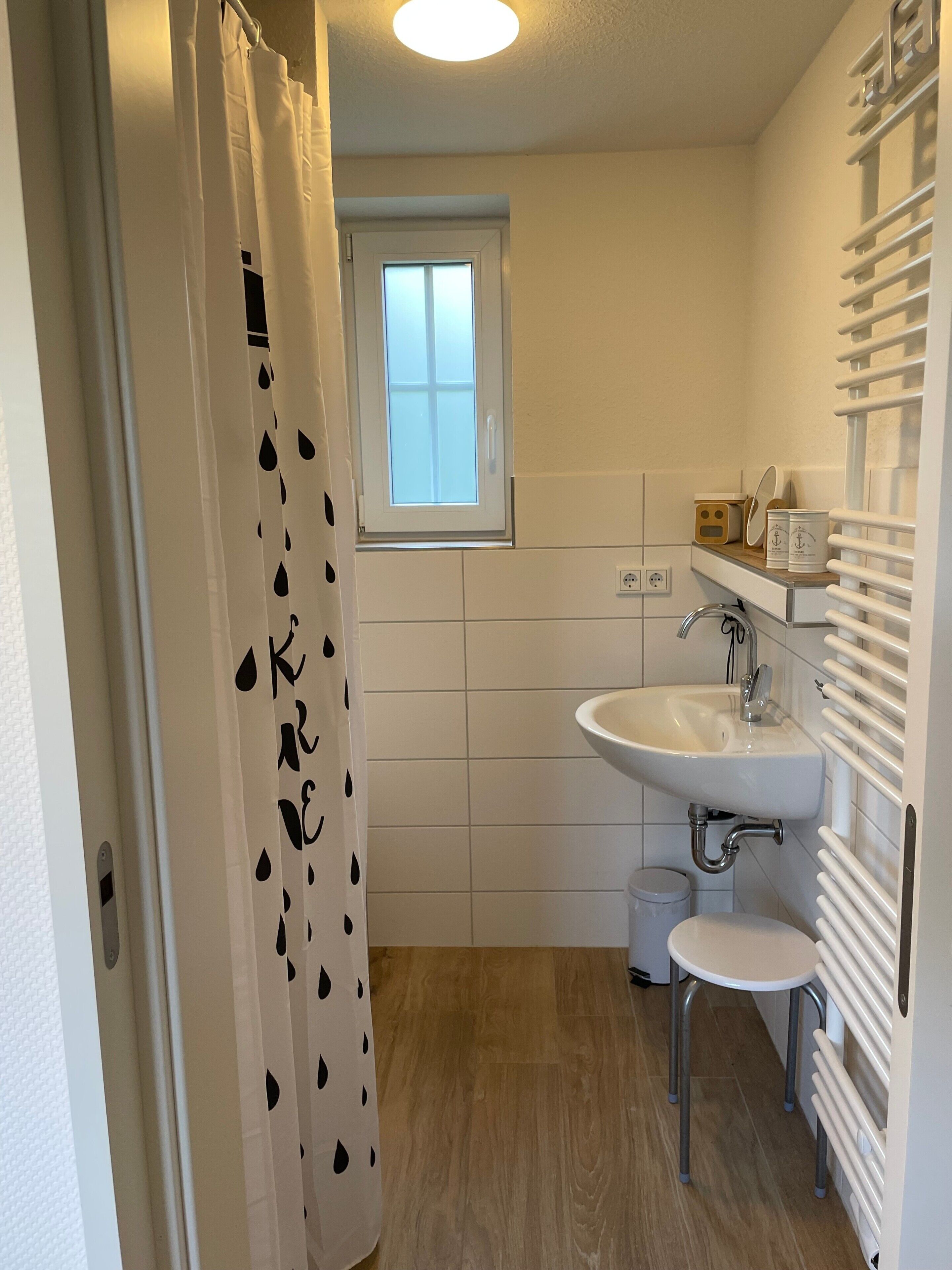Ein Badezimmer mit Duschvorhang, Fenster, Waschbecken, Toilette und Handtuchhalter.